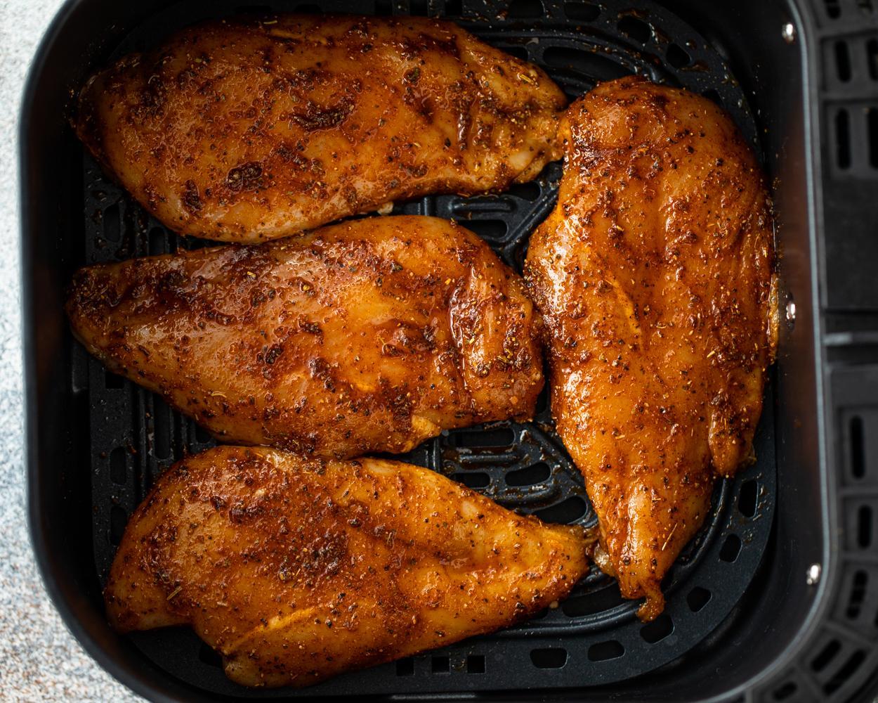 Seasoned chicken breasts in an air fryer basket